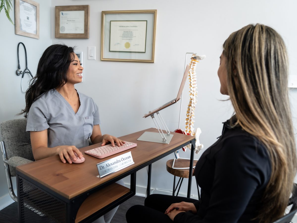 Dr. Alexandra Occean at her desk, in front of her diplomas, with a patient